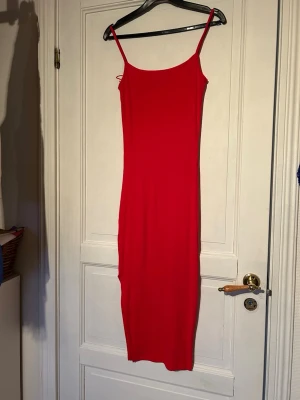 Röd långklänning med slits - Säljer en snygg röd långklänning med smala axelband och slits på sidan. Stretchigt material. Använd men i fint skick! 