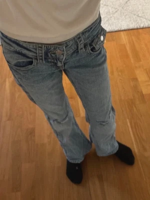 Bootcut jeans i ljusblå denim - Säljer ett par bootcut jeans i ljusblå tvättad denim med slitningar på knäna och snygga detaljer på bakfickorna. Byxorna har låg midja och klassisk femficksdesign. Från gina tricot young storlek 146. Använda 2 gånger