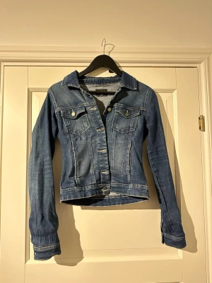 Blå jeansjacka från ONLY, S - Snygg blå jeansjacka från ONLY i storlek small. Klassisk modell med krage, två bröstfickor med knappar och långa ärmar. Stretchig i materialet.
