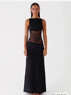 Svart långklänning med spetsdetaljer - Supersnygg svart långklänning med transparent spets i midjan och öppen rygg. Klänningen är ärmlös och har en tight passform upptill som övergår i en rak kjol. Perfekt för dig som vill sticka ut med en elegant och modern look.