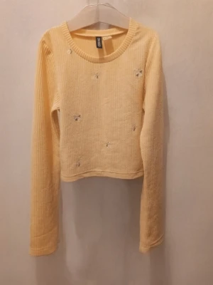 Beige ribbad långärmad topp från H&M  - Säljer en beige ribbad långärmad topp från H&M. Toppen har små broderade blommor i vitt, gul och grön på framsidan och är croppad i modellen. Perfekt att styla med jeans eller kjol för en chill look.