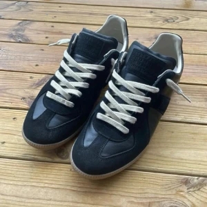 Maison margiela Gats - Maison Margiela sneakers i svart skinn och mocka med kontrasterande vita snören och beige innersida. Snygg gummisula i brunt och klassisk rund tå. Perfekt för dig som gillar stilrena och tidlösa sneakers med coola detaljer.