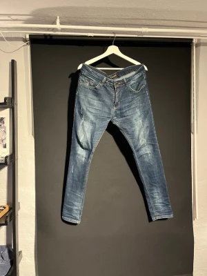 Blå Fashion Jeans slim fit - Säljer ett par blå Fashion Jeans med slim fit och klassisk femficksdesign. Jeansen har slitningar och ljusare partier på benen för en cool, använd look. Materialet är jeans med kontrastsömmar och normal midja. Perfekt för dig som gillar en smal siluett.