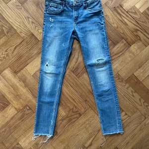 Blå skinny jeans med slitningar - Snygga blå skinny jeans med slitningar på knäna och fransiga benslut. Klassisk femficksmodell med cool regnbågsfärgad söm på bakfickorna. Perfekt passform för dig som gillar smala ben och streetstyle.