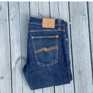Mörkblå Nudie Jeans med gul söm - Snygga mörkblå jeans från Nudie Jeans med klassisk gul vågsöm på bakfickorna och brunt läderpatch i midjan. De säljs pågrund av att dom var för små. De är i oanvänt skickt och finns ings deffekter. Nypris ligger runt 1500 så de är ett bra pris till kvaliten. Storlek 33/32