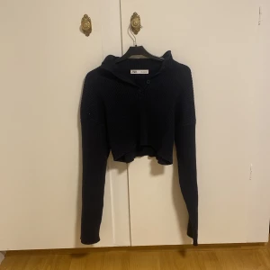 Marin blå croppad stickad hoodie från Zara - Säljer en marin blå croppad stickad hoodie från Zara med långa ärmar och huva. Tröjan har ribbad struktur och knappar framtill vid halsen. Perfekt för lager-på-lager och chill dagar. Pris kan diskuteras