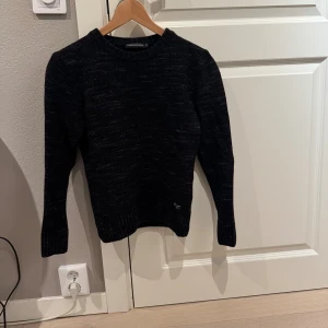 Svart stickad tröja Peak Performance  - Mysig svartmelerad stickad tröja från Peak Performance i storlek S. Tröjan har rund halsringning, ribbade muddar och lång ärm. Perfekt för kyliga dagar. Krympt i tvätten så sitter som en xxs!!