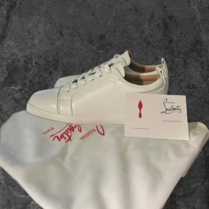 Vita skor från Christian Louboutin - Säljer ett par stilrena vita sneakers från Christian Louboutin med klassisk röd sula och guldfärgad logga på innersulan. Skorna har snörning, rund tå och är tillverkade i slätt skinn. Perfekt för dig som gillar exklusiva detaljer och clean look.
