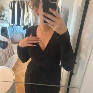 Svart omlottopp med knyt - Snygg svart långärmad omlottopp med v-ringning och knyt i midjan. Toppen har en elegant och figurnära passform som framhäver siluetten. Perfekt för dig som gillar stilrena och klassiska plagg med en modern twist.