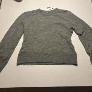 Grå stickad tröja från H&M - En enkel och snygg grå stickad tröja från H&M i storlek S, passar allt från xs till M beroende på hur tight man vill att tröjan ska sitta. Tröjan har rund hals, ribbade muddar vid ärmslut och nederkant samt lång ärm. Perfekt för dig som gillar en clean och chill stil under höst och vinter.