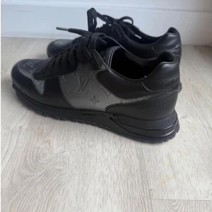 Louis Vuitton skor - Svarta Louis Vuitton sneakers i skinn med klassiskt LV-monogram i grått på sidor och tå. Snygg, chunky sula med LV-logga undertill och bak på hälen. Skorna har snörning och en stilren, sportig vibe som passar till streetwear. Lyxig känsla och ikonisk design. Ny pris 11 tusen säljer för 5 tusen helt äkta skor