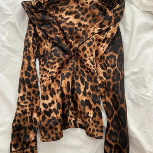 Leopardmönstrad blus med krage - Säljer en snygg leopardmönstrad blus med bred krage och långa ärmar. Blusen har en cool brun och svart färgkombination och är tillverkad i ett glansigt, mjukt material som känns lyxigt. Perfekt för dig som vill sticka ut med ett djuriskt mönster.