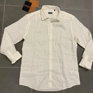 Vit linneskjorta från Zegna XL - Fräsch vit skjorta från Zegna i storlek XL, tillverkad i mjukt linne. Klassisk krage, långärmad och med knappar framtill. Perfekt för dig som gillar stilrena och luftiga plagg. Snygg passform och enkel att matcha med dina favoritjeans eller shorts.