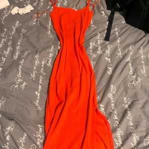 Röd långklänning med smala axelband - Säljer en snygg röd långklänning med smala axelband och figurnära passform. Klänningen har en enkel och stilren design, perfekt för dig som gillar att sticka ut med färg. Materialet känns mjukt och följsamt mot kroppen. Passar S/M