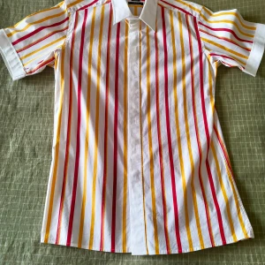 Randig kortärmad skjorta från Esprit - Kortärmad skjorta från Esprit med vita, röda och gula vertikala ränder. Skjortan har klassisk krage, dold knäppning framtill och är tillverkad i stretchigt bomullsmaterial. Perfekt för dig som gillar färg och vill sticka ut lite extra!