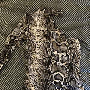Snakeprint klänning från Gina Tricot - Supersnygg kort klänning från Gina Tricot i XS med ett coolt ormskinnsmönster i svart, grått och beige. Klänningen har lång ärm och figurnära passform, perfekt för dig som gillar att sticka ut med djurmönster. Materialet är mjukt och stretchigt polyester.