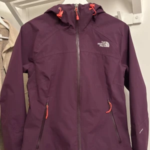 Mörklila skaljacka från The North Face - Mörklila vindjacka från The North Face med orangea detaljer på dragkedjor och snörning. Köpt på Vinted men tyvärr för liten, skulle säga att den sitter som en S 🙌⚡️