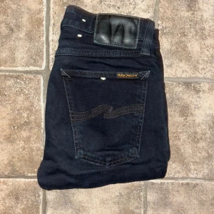 Nudie Jeans - Snygga svarta Skinny Lin jeans från Nudie Jeans med klassisk femficksdesign och coola sömmar på bakfickorna. Jeansen är tillverkad i stretchig bomull med 2% elastan för extra komfort. Midja 33cm, längd 94cm.  Ifall det inte finns någon bild i annonsen där jag bär plaggen jag säljer så är det för att jag ej kan ha storleken heller passformen, så kolla måtten för storlek och googla på modellnamnet för passform 😉 s4