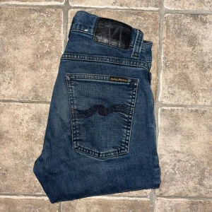 Nudie Jeans  - Snygga mörkblå jeans från Nudie Jeans, modell Tight Terry. Slimmad passform med skinny siluett och klassisk femficksdesign. Tillverkade i ekologisk bomull med stretch för extra komfort. Ikonisk Nudie-brodyr på bakfickorna och svart läderpatch i midjan. Midja 35cm, längd 101cm.  Ifall det inte finns någon bild i annonsen där jag bär plaggen jag säljer så är det för att jag ej kan ha storleken heller passformen, så kolla måtten för storlek och googla på modellnamnet för passform 😉 s4