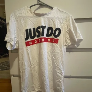 Vit t-shirt med tryck 'Just Do Nothing' - Säljer en vit t-shirt från Country med stort tryck på bröstet där det står 'JUST DO NOTHING' i svart och rött. T-shirten har rund hals och korta ärmar. Materialet är mjuk bomull och passformen är normal. Perfekt för chill dagar och statement-look.