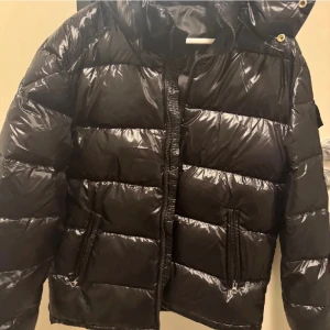 Svart Moncler pufferjacka med huva - Säljer en svart, glansig pufferjacka från Moncler med huva och dragkedja framtill. Jackan har två fickor med dragkedja och en Moncler-logga på ärmen. Perfekt för kalla dagar. Fick en annan jacka i present så har ingen användning för denna som jag köpte för en vecka sen så den är som oanvänd. kom privat för fler bilder om de behövs 