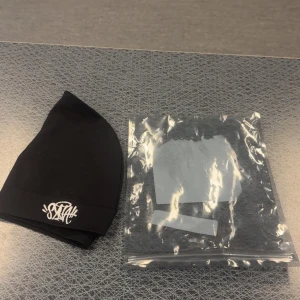 Svart mössa med vit broderad logga - Svart mössa från syna world med vit broderad logga framtill. Mössan har en enkel, tight passform och är tillverkad i mjuk bomull. Perfekt för dig som gillar streetwear och vill ha en clean look med en snygg detalj.