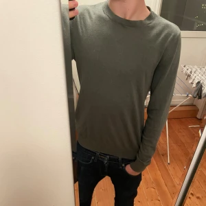 Grön långärmad tröja Dressmann S - Snygg grön långärmad tröja från Dressmann i storlek S. Tröjan har en enkel och stilren design med rund hals och ribbade muddar. Tillverkad i mjuk supima bomull som känns skön mot huden. Perfekt att matcha med jeans eller chinos.