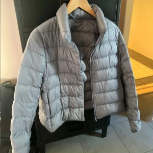 Grå pufferjacka med dragkedja - Säljer en grå pufferjacka med quiltad design och hög krage. Jackan har dragkedja framtill och är perfekt för kyliga dagar. Den har en modern, lite boxig passform och är lätt att matcha med olika outfits.