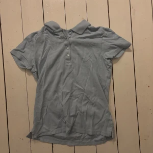 Ljusblå piké t-shirt med krage - Snygg ljusblå piké t-shirt med klassisk krage och tre knappar framtill. Kortärmad och tillverkad i mjuk bomull som känns skön mot huden. Perfekt för dig som gillar enkel och stilren design.