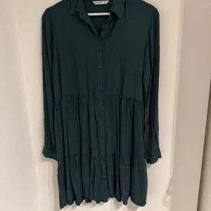 Stradivarius grön klänning, storlek S - No sign of use. Grön klänning med långa ärmar och knappar framtill. Klänningen har en krage och en vågig nederkant.