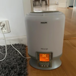 Philips Wake-up Light - Philips Wake-up Light väckarklocka med simulerad soluppgång och digital display. Fungerar som både lampa och alarm, perfekt för naturlig uppvakning. Enheten är i gott skick utan synliga skador eller slitage. Alla knappar och display fungerar som de ska.