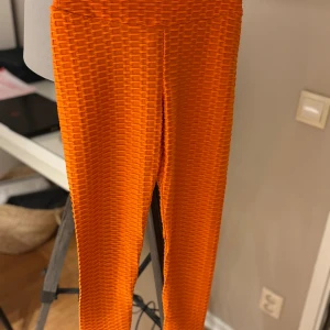 Orange leggings från Amisu XS - Säljer ett par orangea leggings från Amisu i storlek XS. De har en cool texturerad yta och scrunch-detalj bak för extra effekt. Stretchigt syntetmaterial som sitter tight och framhäver formen. Perfekta för dig som vill sticka ut med färg och mönster.