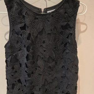 Svart blommig spets topp - Svart topp från Crocker Apparel med snyggt blommigt spetsmönster framtill och slät baksida. Toppen är ärmlös och har en dragkedja i ryggen. Perfekt för dig som gillar detaljer och vill sticka ut lite extra.