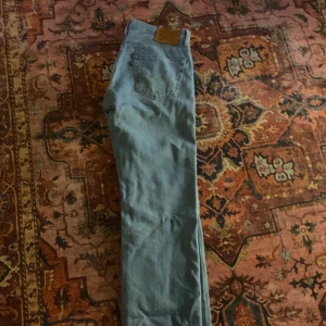 Levi's 501 ljusblå jeans W33 L34 - Ljusblå Levi's 501 Premium jeans med klassisk femficksdesign och raka ben. Jeansen har en snygg vintagekänsla, ikonisk läderpatch bak och är tillverkade i slitstarkt bomullsdenim. Perfekta för dig som gillar tidlös stil och vill ha ett par riktigt schyssta jeans.