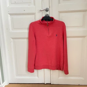 Rosa half zip tröja från Polo Ralph Lauren - Snygg rosa långärmad tröja från Polo Ralph Lauren med half zip och klassisk broderad logga på bröstet. Tröjan har en avslappnad passform och är perfekt för lager-på-lager. Tillverkad i mjuk bomull som känns skön mot huden.