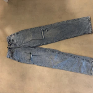 Blå ripped jeans från Divided - Säljer ett par ljusblå jeans från Divided med raka ben och slitna detaljer på låren och knäet. Jeansen har klassisk femficksdesign och är tillverkade i bomull. Perfekta för en avslappnad och trendig look. Endast använda en gång då de är för långa för mig. Hör av er vid frågor💕