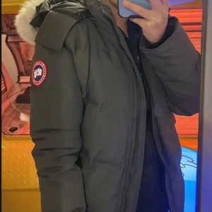 Svart dunjacka från Canada Goose - Säljer en svart dunjacka från Canada Goose med klassisk patch på ärmen och fluffig päls på huvan. Jackan har dragkedja framtill och är designad för att hålla dig varm under kalla vinterdagar. Perfekt för dig som vill ha både stil och funktion.