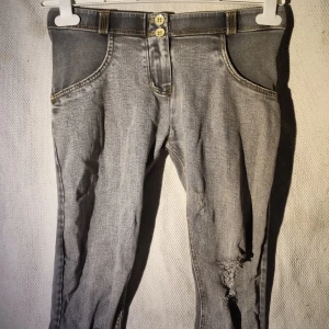 Grå skinny jeans från Freddy WR.UP - Snygga grå skinny jeans från Freddy WR.UP med slitna detaljer på benen och dubbla knappar i midjan. Byxorna har kontrastsömmar i gult och klassiska bakfickor. Stretchigt material som sitter tajt och formar kroppen.