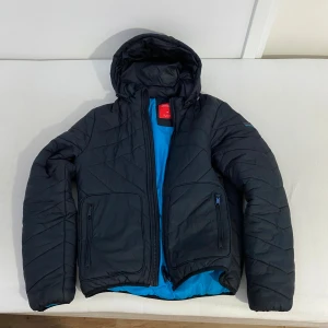 Svart jacka från Björn Borg - Svart jacka från Nike med huva och vit logga på bröstet. Jackan har quiltad design, dragkedja framtill och långärmade ärmar. Perfekt för kalla dagar och har en clean, sportig look som funkar till streetwear. Priset kan diskuteras!