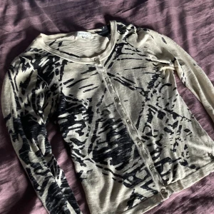 Mönster kofta - Mönstrad kofta i svart och beige i tunnt material, perfekt för både uppklädda och avslappnade tillfällen. Väl använd och har troligtvis bidragit ytterligare en smula till det tunna tyget. I bra skick annars med alla knappar och den är väldigt passande till höst och vår