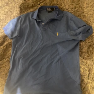 Blå pikétröja från Ralph Lauren - Klassisk blå pikétröja från Ralph Lauren med korta ärmar och krage. Tröjan är i bra skick och storleken medium