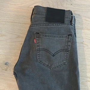 Levi's grå jeans straight fit - Snygga grå jeans från Levi's med klassisk femficksdesign och raka ben. Jeansen har en mörk tvätt, tydliga sömmar och den ikoniska Levi's-taggen på bakfickan. Perfekta för en clean och stilren look. W30 L 34