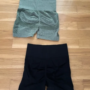 Två par seamless träningsshorts - Säljer två par seamless shorts med hög midja, perfekta för gymmet eller yoga. Ett par är svarta och det andra är gröna. Båda har scrunch-detalj bak för snygg passform och är tillverkade i stretchigt syntetmaterial som andas.
