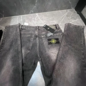 Grå jeans från Stone Island - Säljer ett par grå jeans från Stone Island med klassisk patch på bakfickan och snygga detaljer. Jeansen har rak passform och är tillverkade i slitstarkt bomullsmaterial. Perfekt för dig som gillar streetwear och vill ha något som sticker ut.