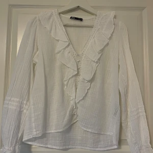 Vit volangskjorta från Zara - Supersöt vit skjorta från Zara i storlek XS med v-ringning, volanger och spetsdetaljer framtill. Den är i väldigt bra skick och säljer då den inte kommee till användning längre.