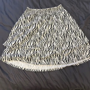 Zebramönstrad kortkjol från XOXO Friends - Supersnygg kortkjol med zebramönster från XOXO Friends. Kjolen har volangkant och resår i midjan.. Den är svartvit och har en luftig känsla, perfekt för att sticka ut med en cool look.