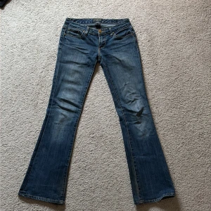 Blå bootcut jeans från Seven7 - Snygga blå bootcut jeans från Seven7 med klassisk femficksdesign och broderade bakfickor. Jeansen har låg midja och är tillverkade i bomull, polyester och spandex för en skön stretch. Perfekt för dig som gillar en retroinspirerad look. Säljer jeansen då dom tyvärr blivit för små för mig! 