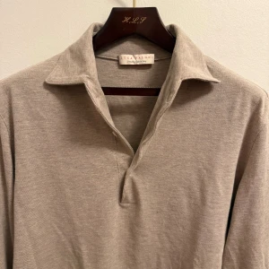 Luca Faloni polo - Snygg beige pikétröja från Luca Faloni i 100% bomull. Tröjan har klassisk krage, v-ringad öppning med tre knappar och långa ärmar med manschett och två knappar. Perfekt för dig som gillar stilrena och tidlösa plagg.