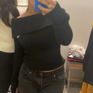 Svart offshoulder stickad topp H&M  - Säljer en svart stickad offshoulder topp från H&M i storlek XS. Toppen har ribbad struktur, lång ärm och en bred krage som vilar snyggt över axlarna. Perfekt för dig som gillar en stilren och trendig look med lite edge.