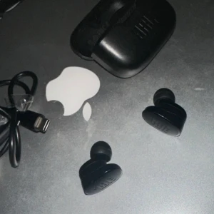 JBL Trådlösa Hörlurar - Snygga svarta JBL trådlösa hörlurar med laddningsetui och USB-C kabel. Hörlurarna och etuiet ser ut att vara i gott skick utan synligt slitage. Perfekt för musik, samtal och träning med bra ljudkvalitet och smidig laddning.